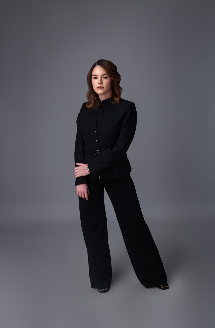 Dana Medina de pie, con traje negro, frente a un fondo gris
